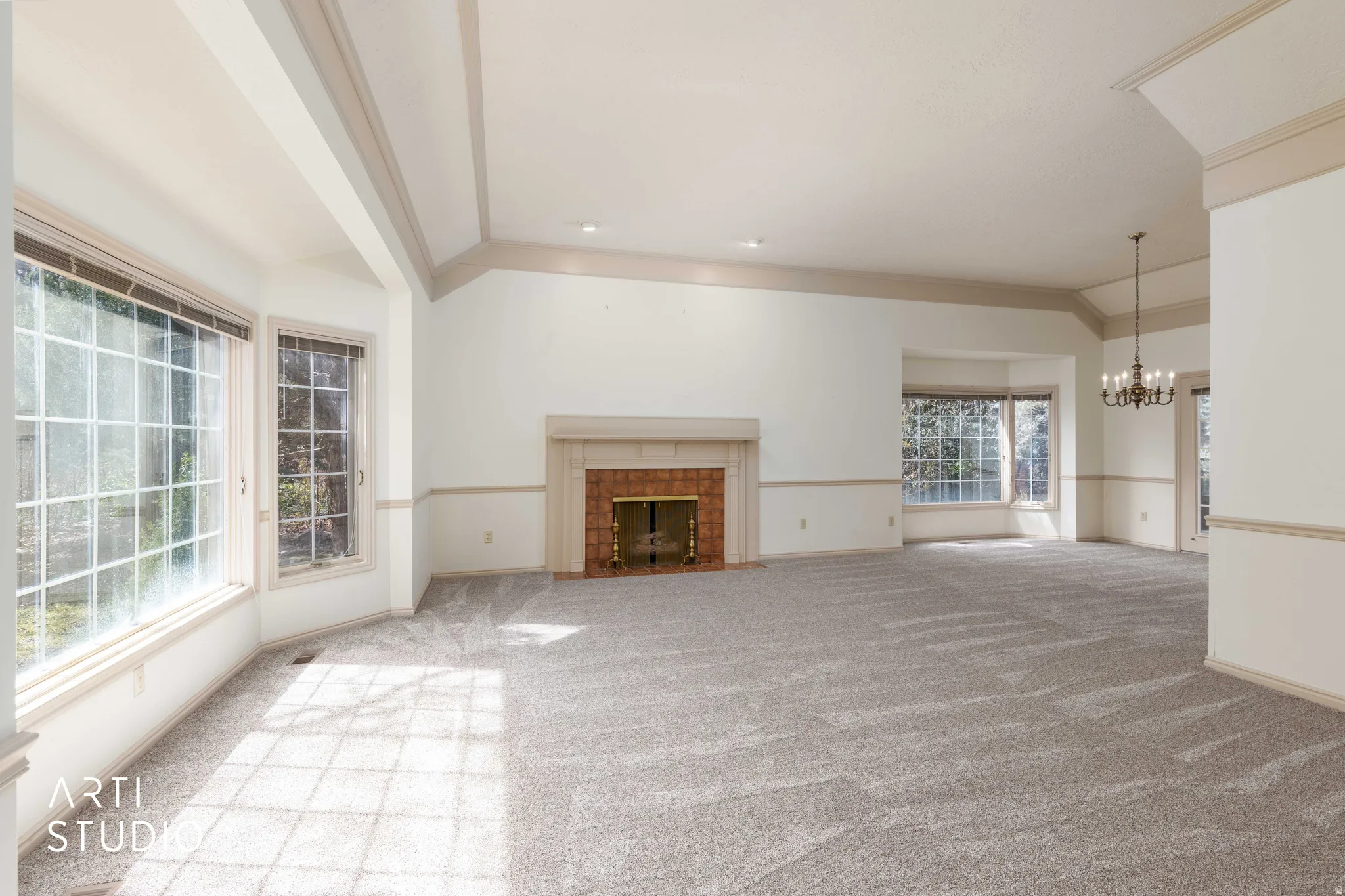 Unfurnished living room with vaulted ceiling with beams, light colored carpet, suspended lighting, and a tiled fireplace