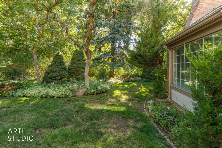 Expansive rear yard featuring mature trees, manicured lawn, established landscaping, and a bay window