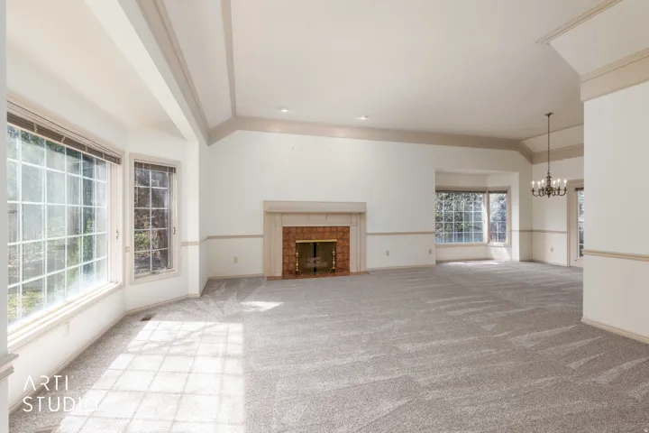 Unfurnished living room with vaulted ceiling with beams, light colored carpet, suspended lighting, and a tiled fireplace