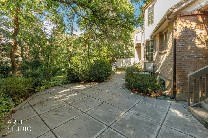 Paved patio area, mature trees, brick exterior, stucco siding, and multi-pane windows