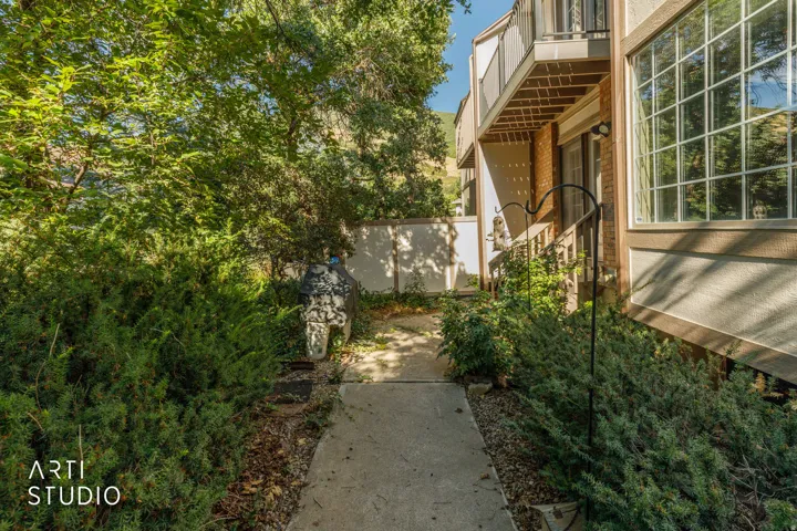 Concrete pathway leading to the entrance, surrounded by dense green shrubbery and mature trees