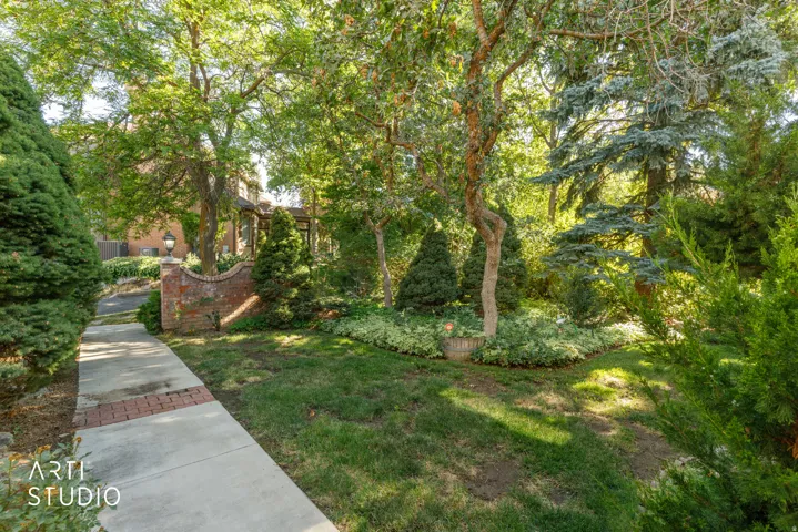 Manicured landscaping featuring mature trees and diverse plantings, a brick and concrete pathway, and a curved brick wall with an attached lantern