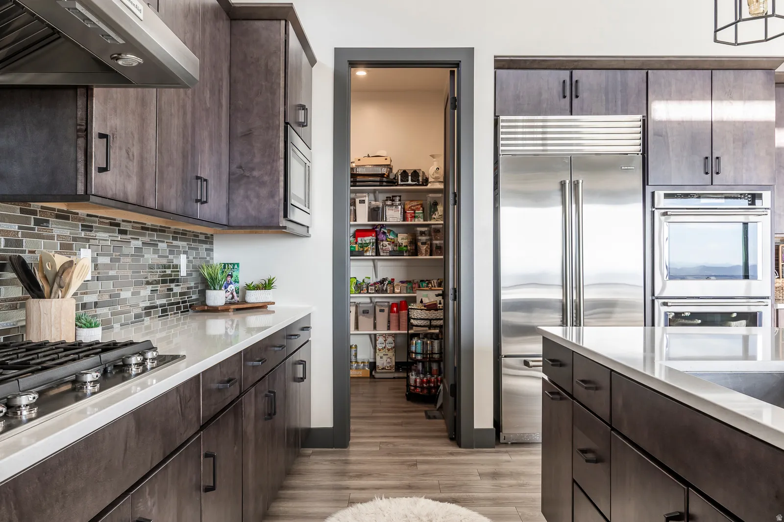 Kitchen featuring dark wood finish cabinetry, exhaust hood, built in appliances, and light wood-style flooring