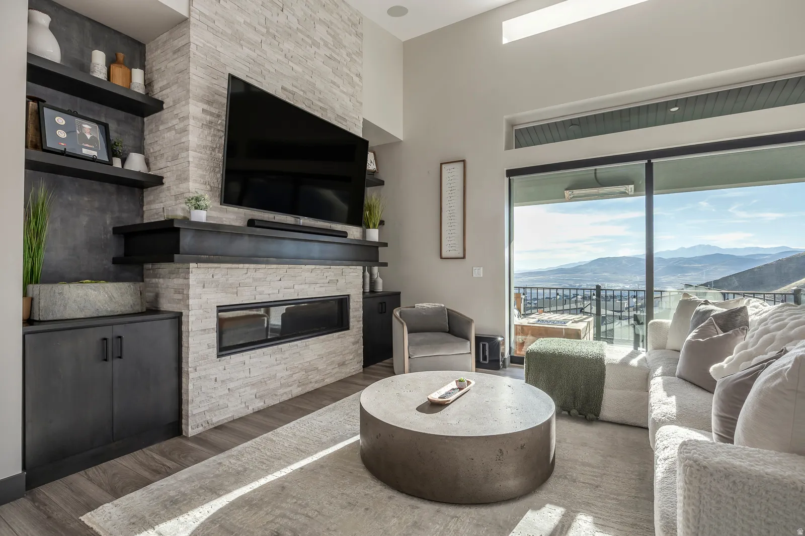 Living room featuring a stone fireplace, wood finished floors, and a high ceiling
