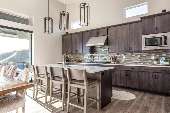 Kitchen with dark wood finish cabinetry, a high ceiling, decorative light fixtures, dark wood-style flooring, and an island with sink