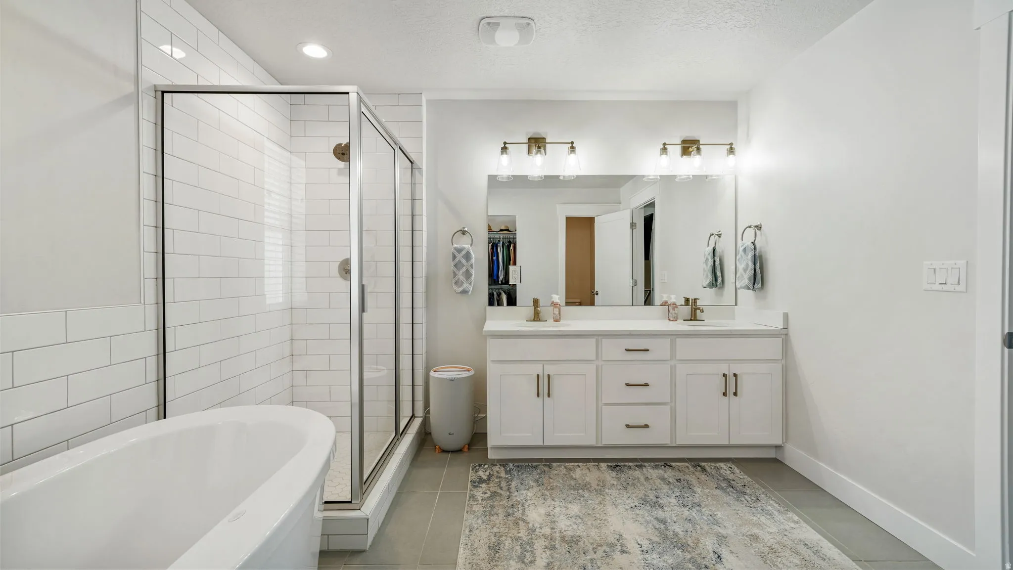 Full bath with a freestanding bath, double vanity, a shower stall, a textured ceiling, and light tile patterned floors