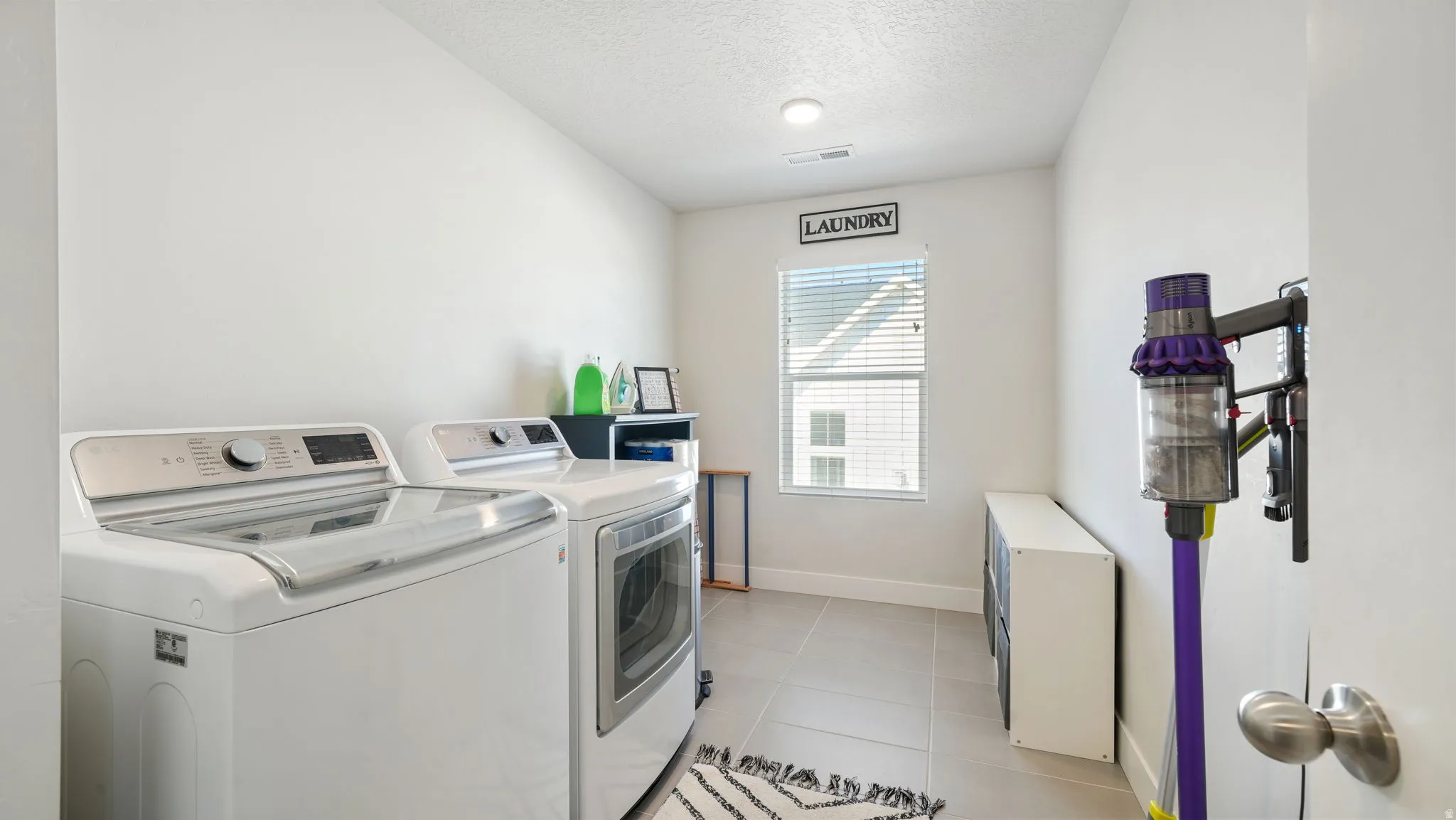 Laundry room with independent washer and dryer, a textured ceiling, and light tile patterned flooring