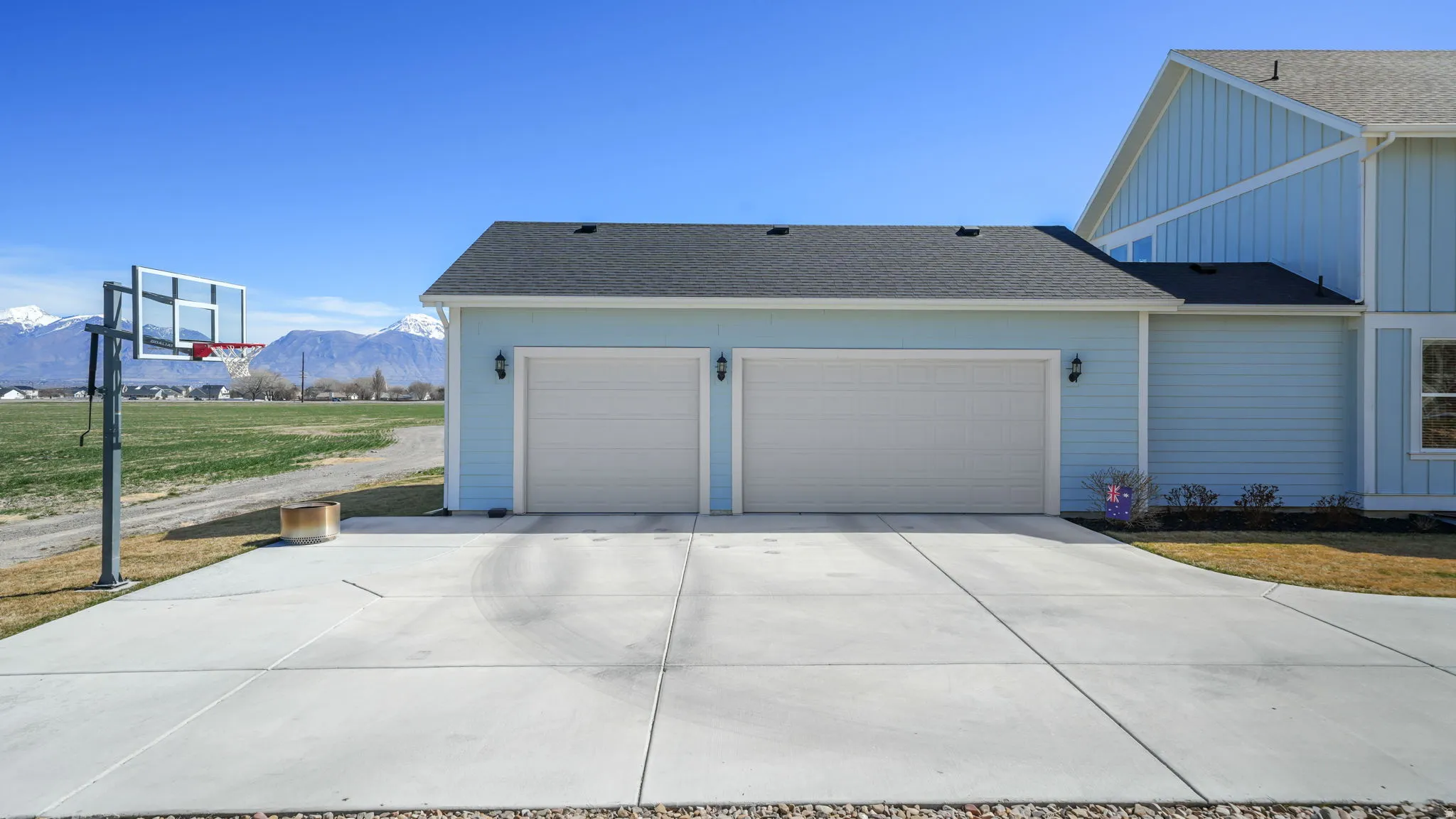 View of side of property with board and batten siding, roof with shingles, a mountain view, a yard, and concrete driveway