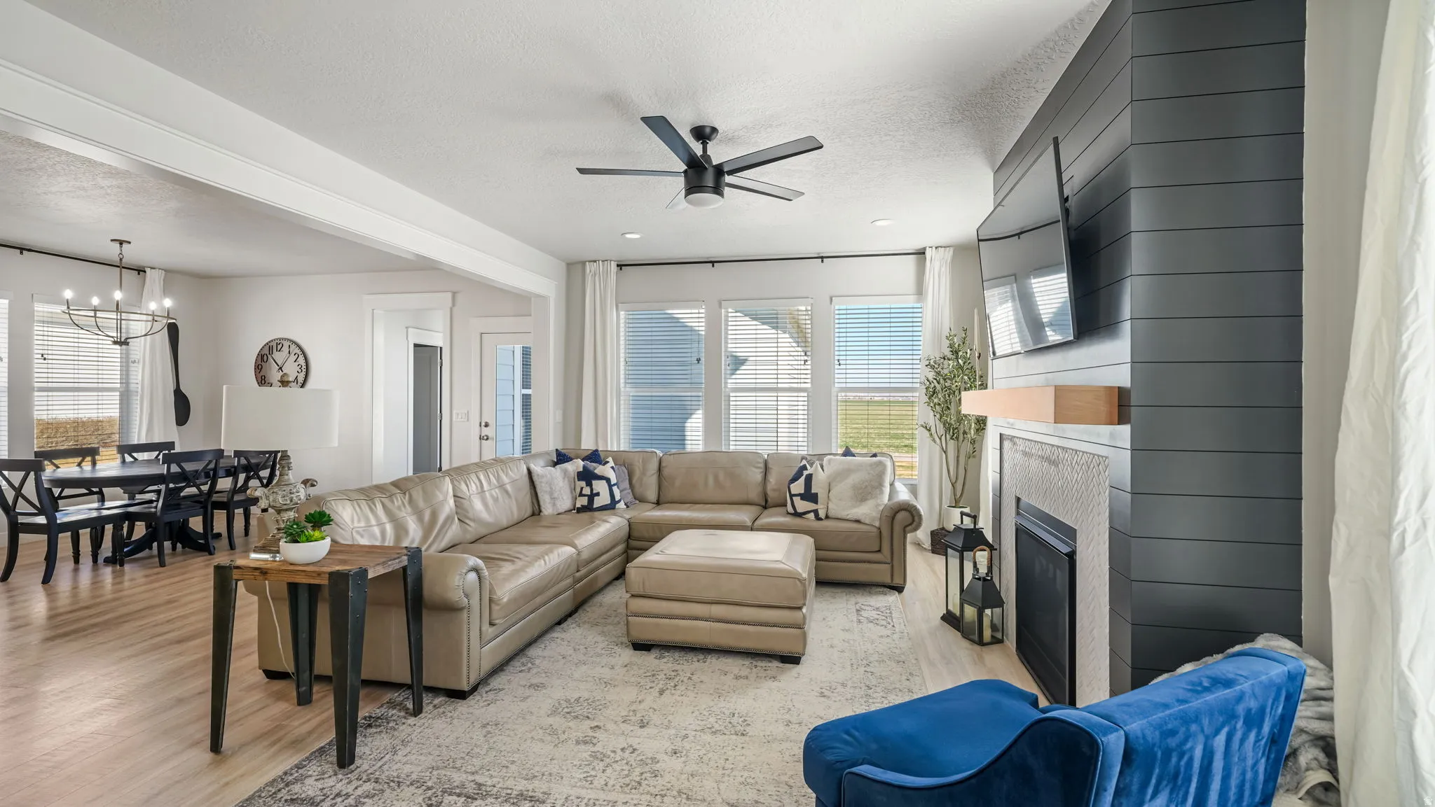 Living area featuring light wood-type flooring, a textured ceiling, ceiling fan, a fireplace, and suspended lighting