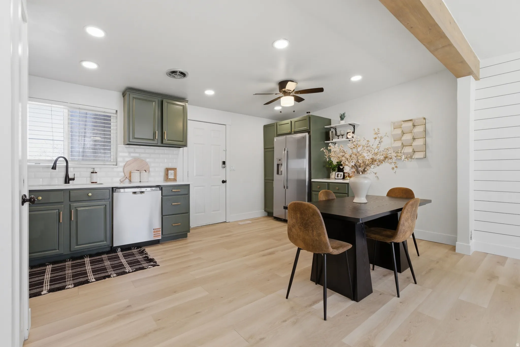 Kitchen with ceiling fan, stainless steel appliances, light wood-type flooring, backsplash, and green cabinetry