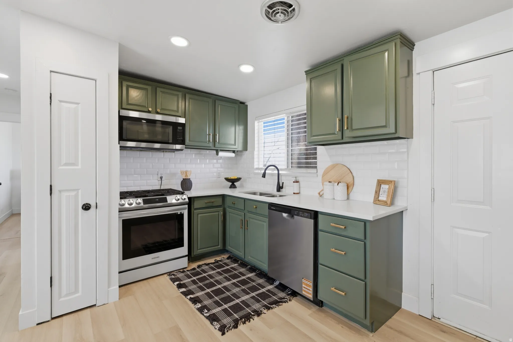 Kitchen with green cabinetry, stainless steel appliances, light stone counters, light wood-type flooring, and backsplash