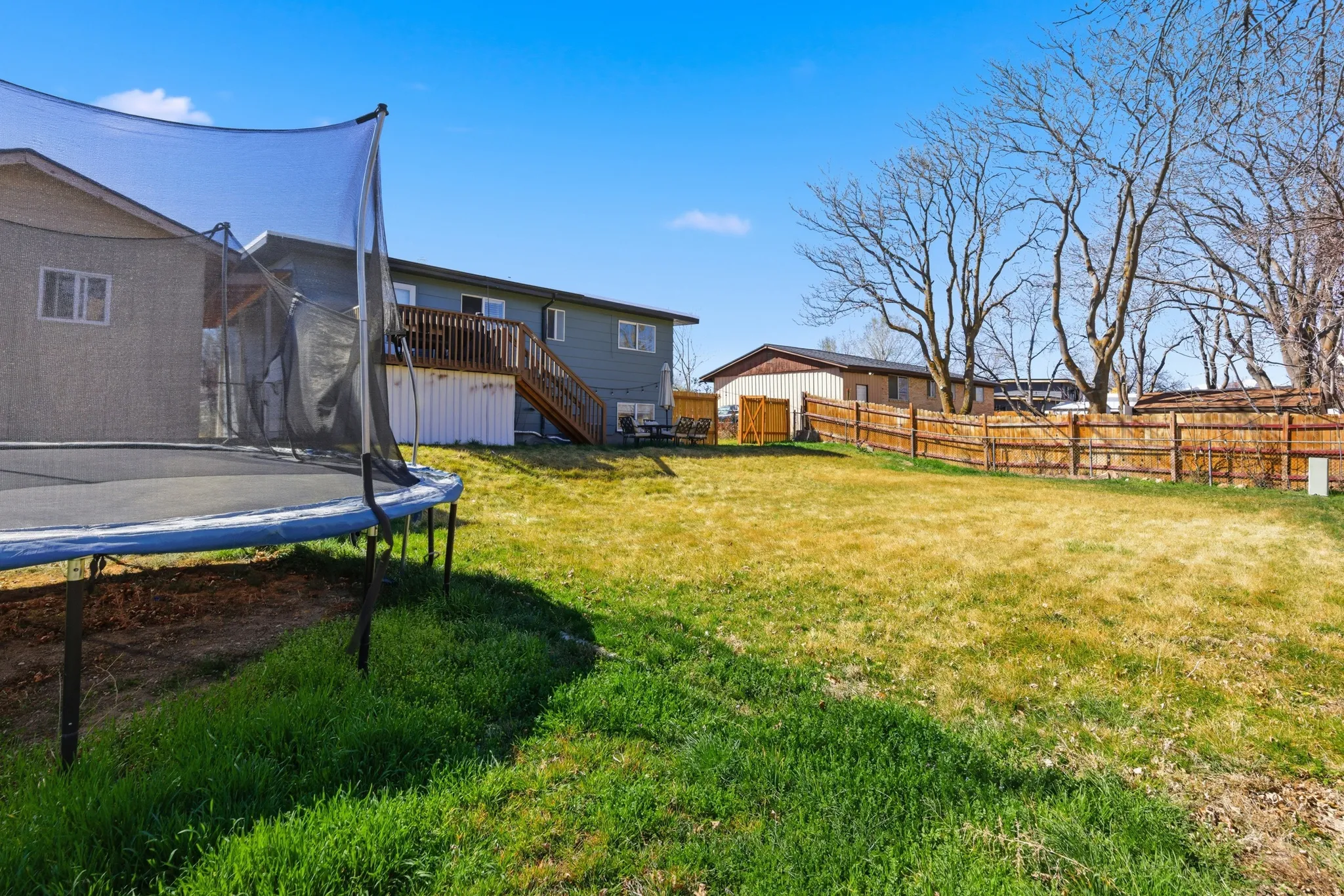 Fenced backyard featuring a trampoline and a wooden deck