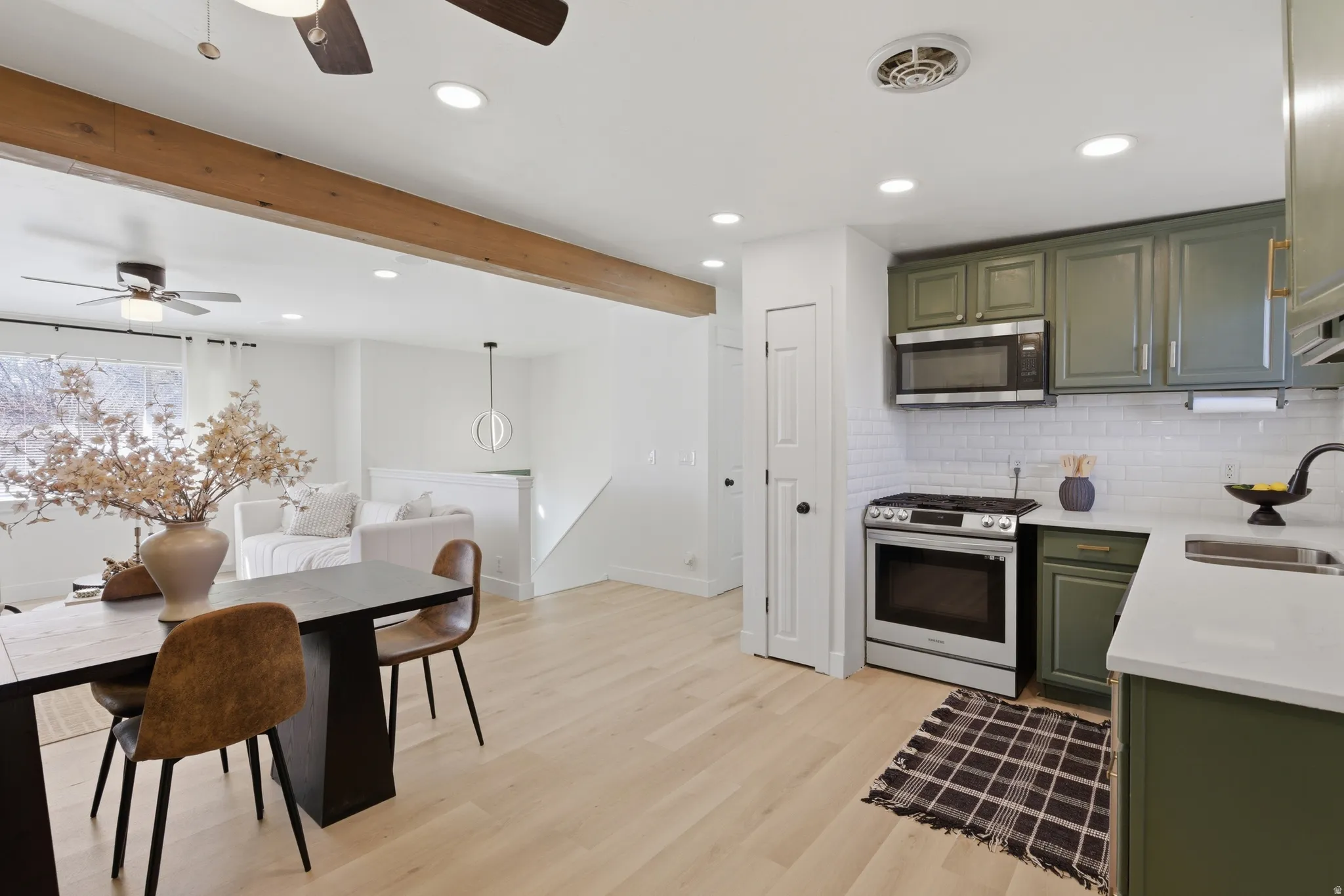 Kitchen with green cabinets, stainless steel appliances, beamed ceiling, light stone counters, and light wood-style flooring
