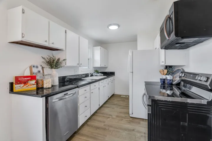 Kitchen with stainless steel appliances, white cabinets, light wood-style floors, and dark countertops