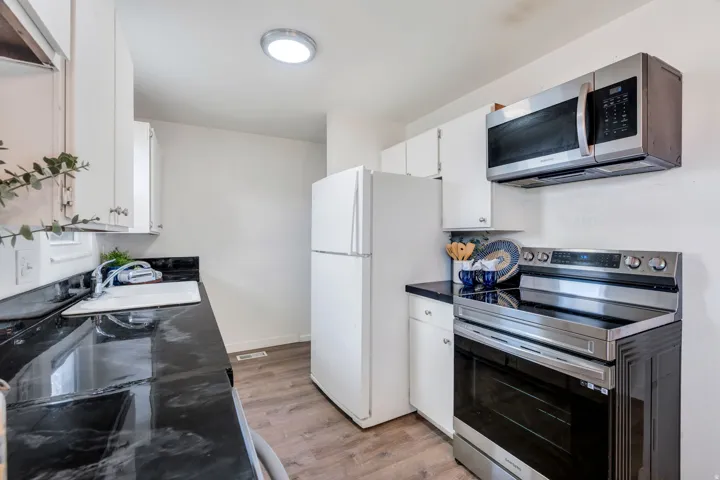 Kitchen with dark countertops, stainless steel appliances, white cabinets, and light wood-style floors