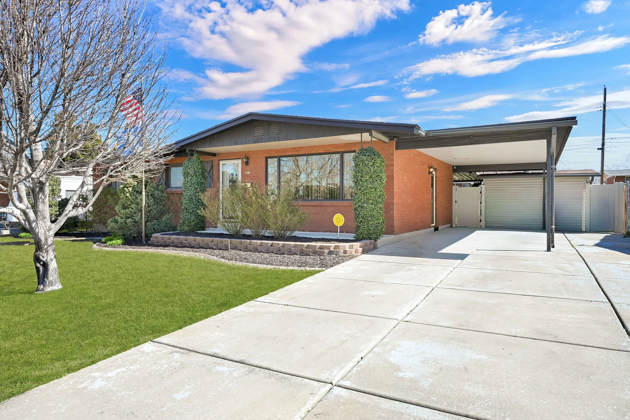 View of front of home with driveway, an attached carport, brick siding, and a front lawn
