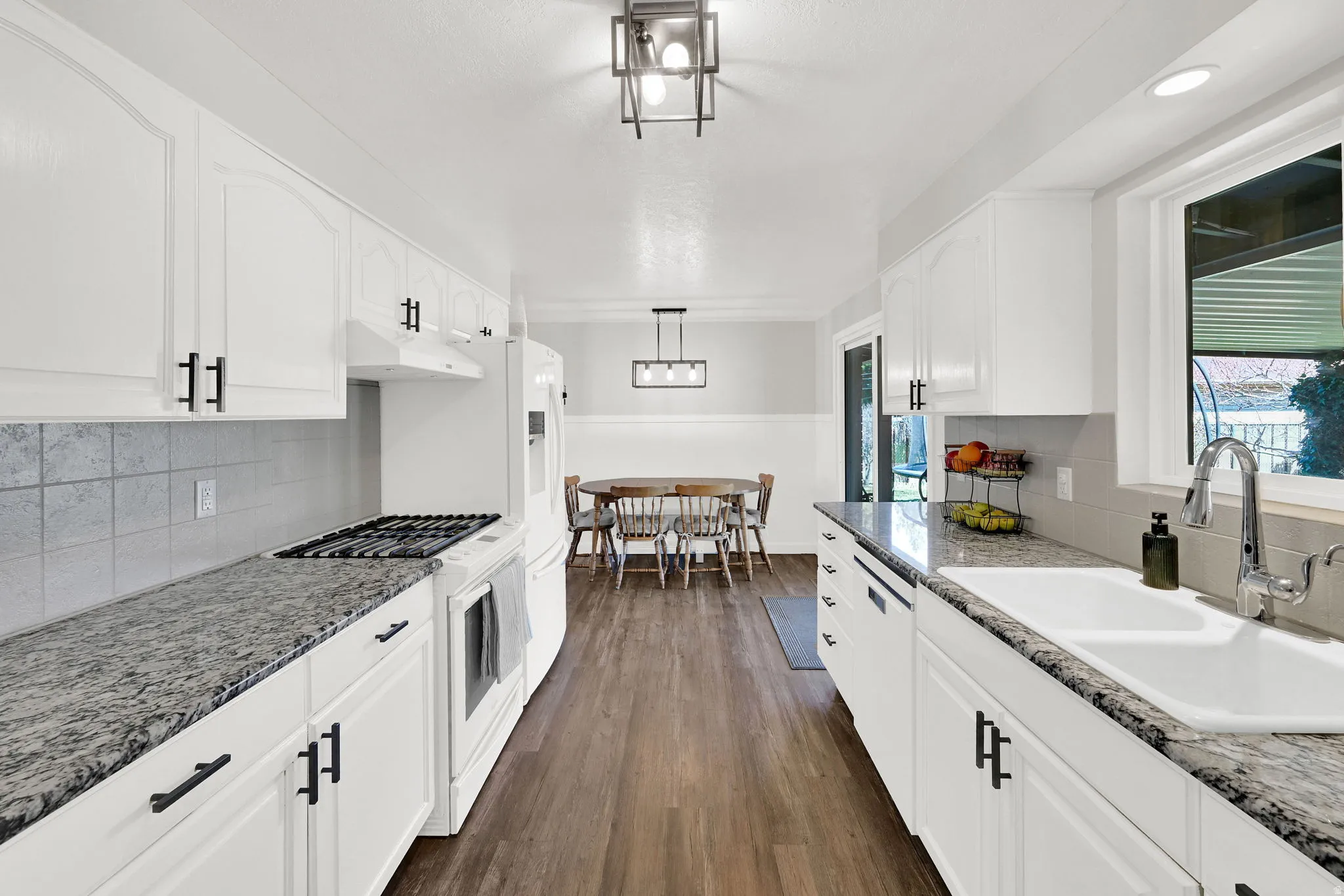 Kitchen with white appliances, backsplash, dark wood-type flooring, and white cabinets