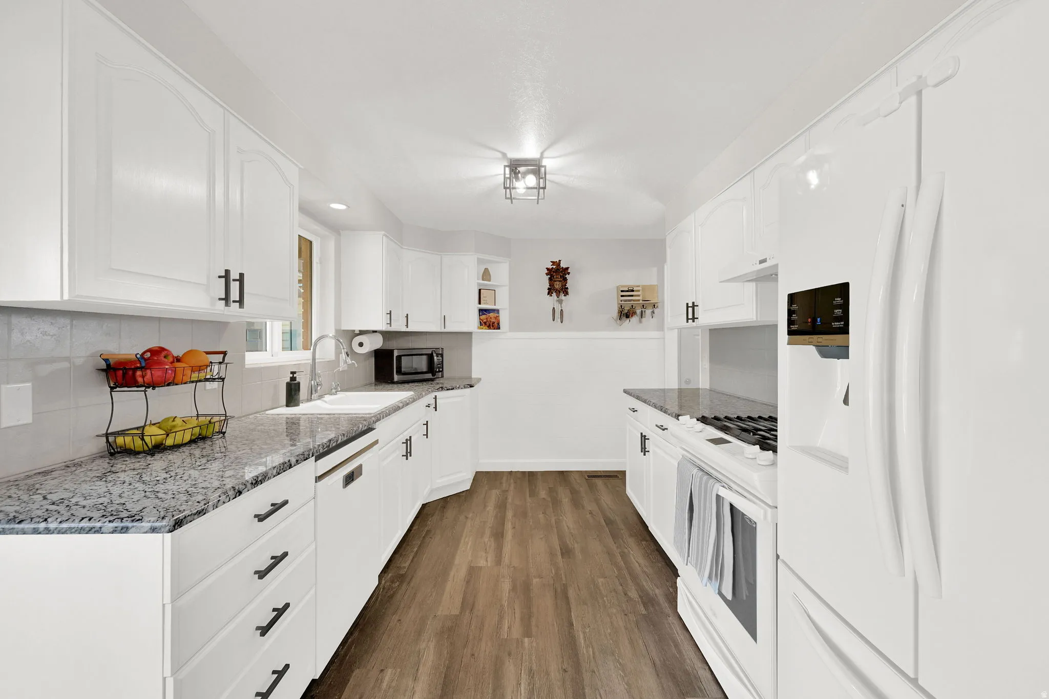 Kitchen with white appliances, white cabinets, dark wood-style flooring, backsplash, and dark stone countertops