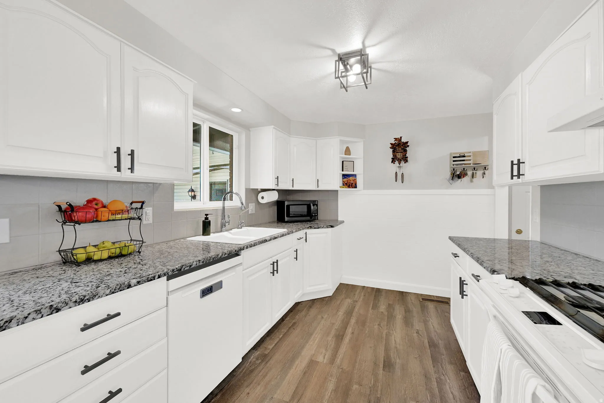 Kitchen with dark stone counters, dishwasher, dark wood-type flooring, white cabinets, and tasteful backsplash