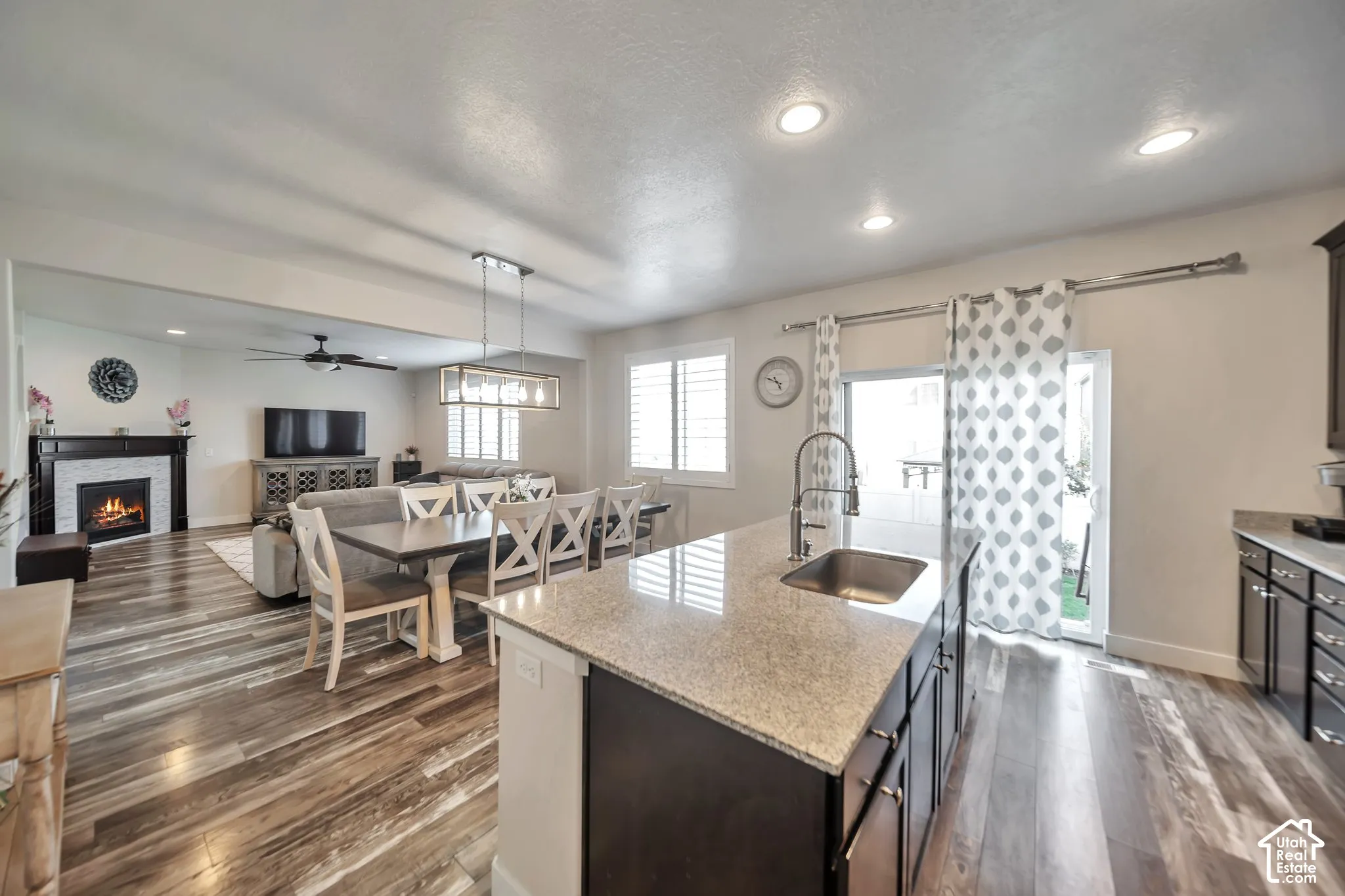 Kitchen featuring pendant lighting, a warm fireplace, light stone counters, open floor plan, and a kitchen island with sink