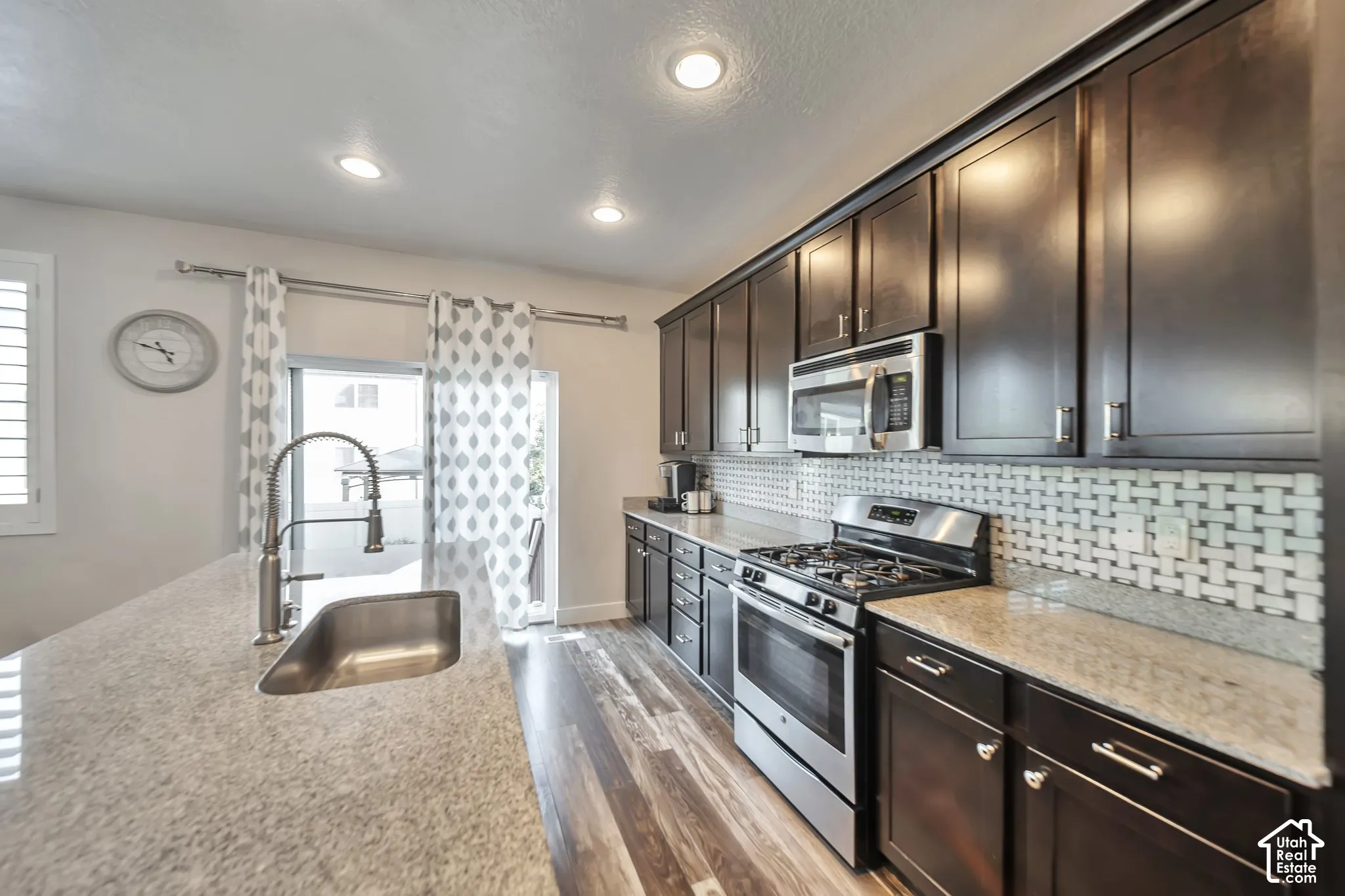 Kitchen featuring stainless steel appliances, light stone counters, light wood-type flooring, dark wood finish cabinets, and decorative backsplash