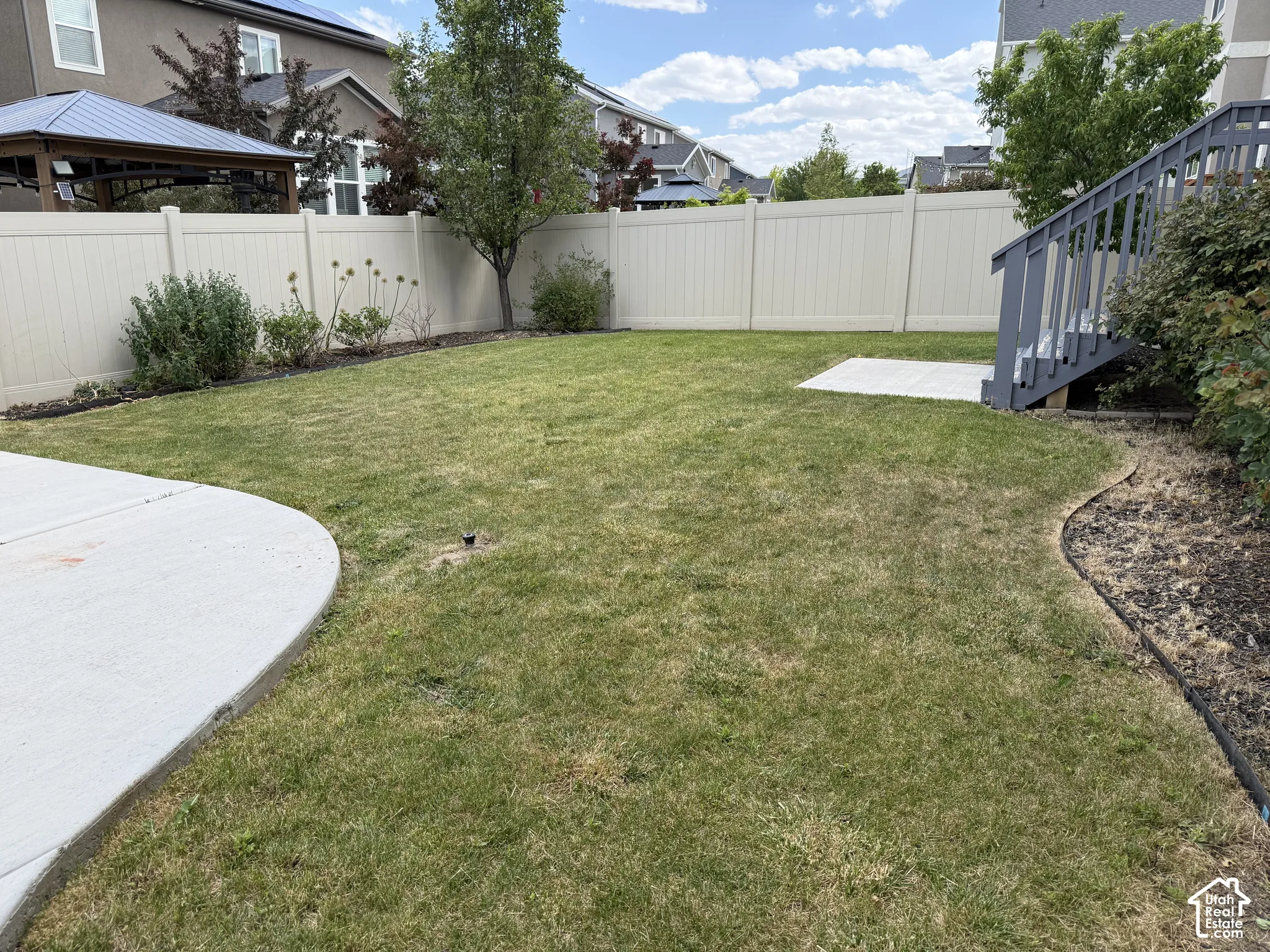 Expansive grassy backyard featuring a light-toned privacy fence, a concrete patio area, and mature perimeter landscaping