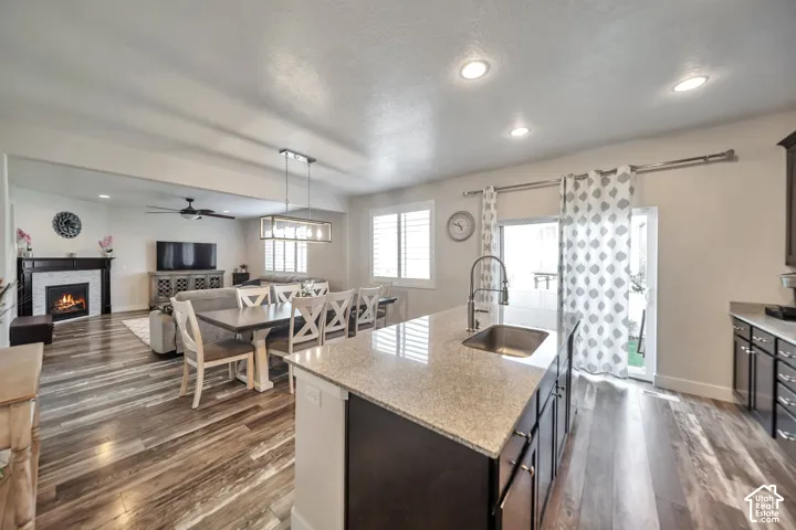 Kitchen featuring pendant lighting, a warm fireplace, light stone counters, open floor plan, and a kitchen island with sink