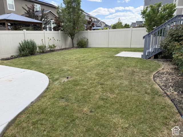 Expansive grassy backyard featuring a light-toned privacy fence, a concrete patio area, and mature perimeter landscaping