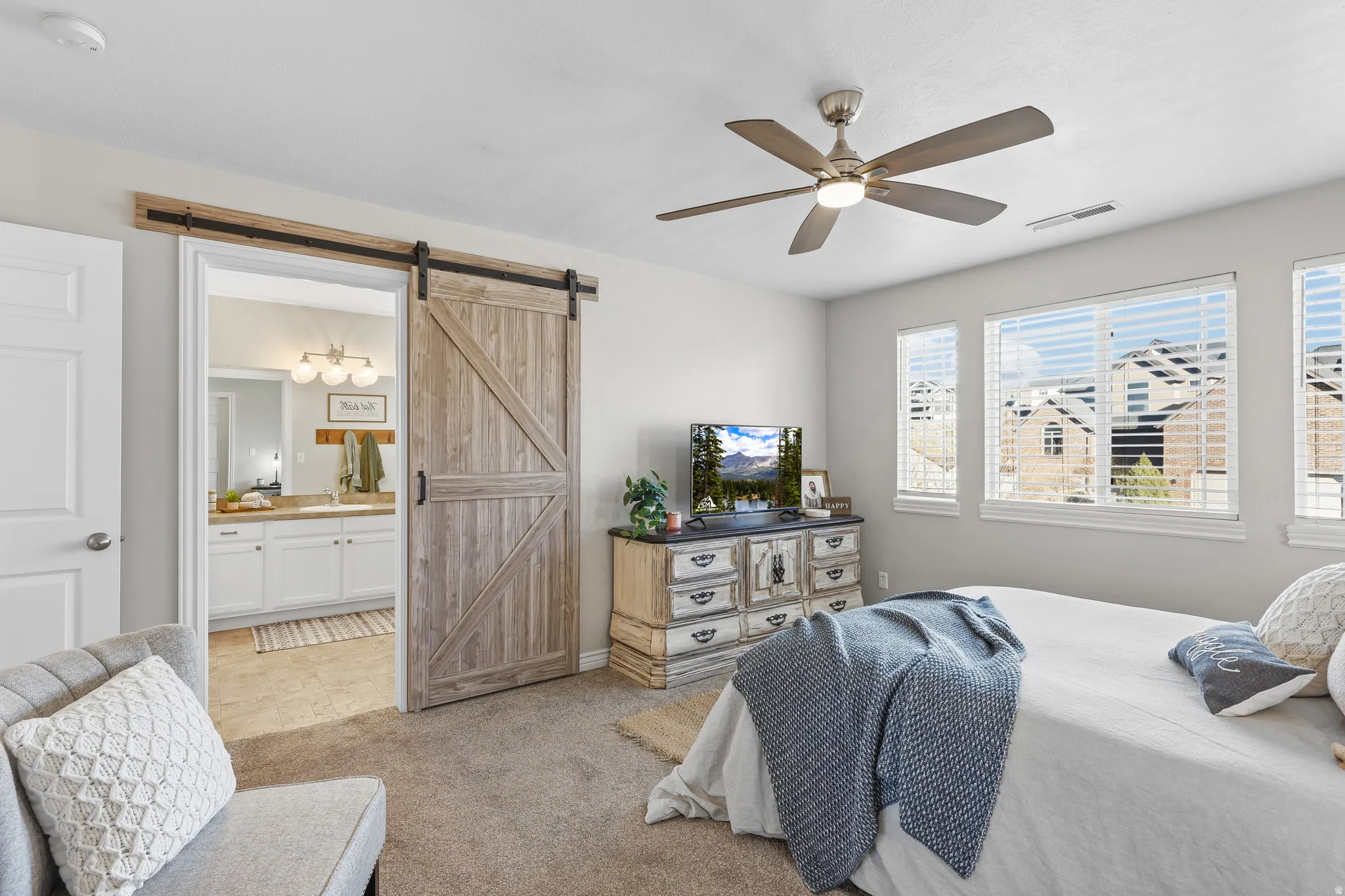 Bedroom featuring a barn door, light carpet, ceiling fan, and ensuite bath
