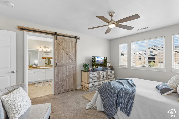 Bedroom featuring a barn door, light carpet, ceiling fan, and ensuite bath