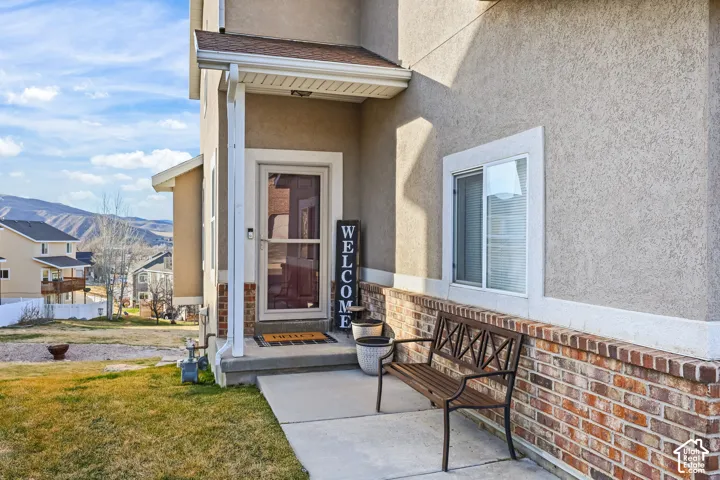 View of exterior entry with stucco siding, a mountain view, and a yard