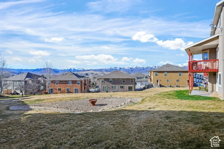 View of grassy yard with a mountain view, a residential view, and a balcony
