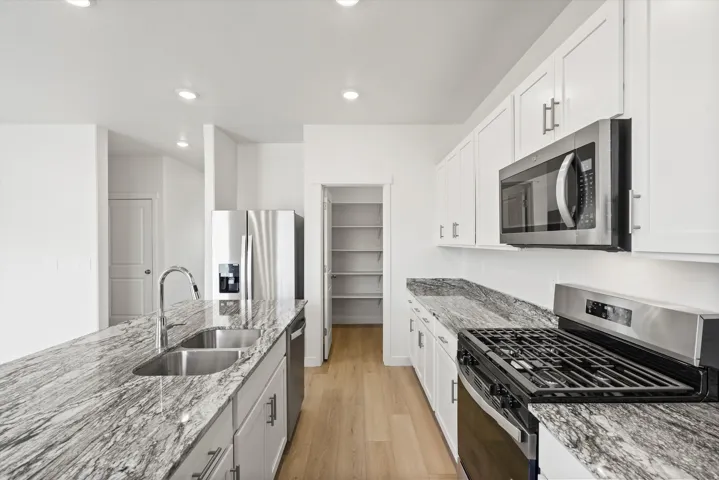 *DISCLAIMER* Interior package and colors may vary.  Kitchen with stainless steel appliances, light wood-style flooring, light stone counters, white cabinets, and recessed lighting