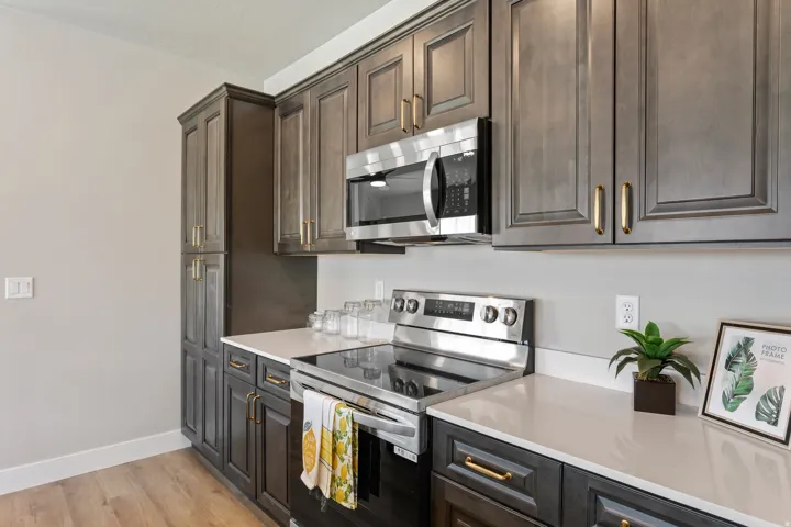 Kitchen featuring stainless steel appliances, light wood-type flooring, dark wood finish cabinetry, and light stone countertops
