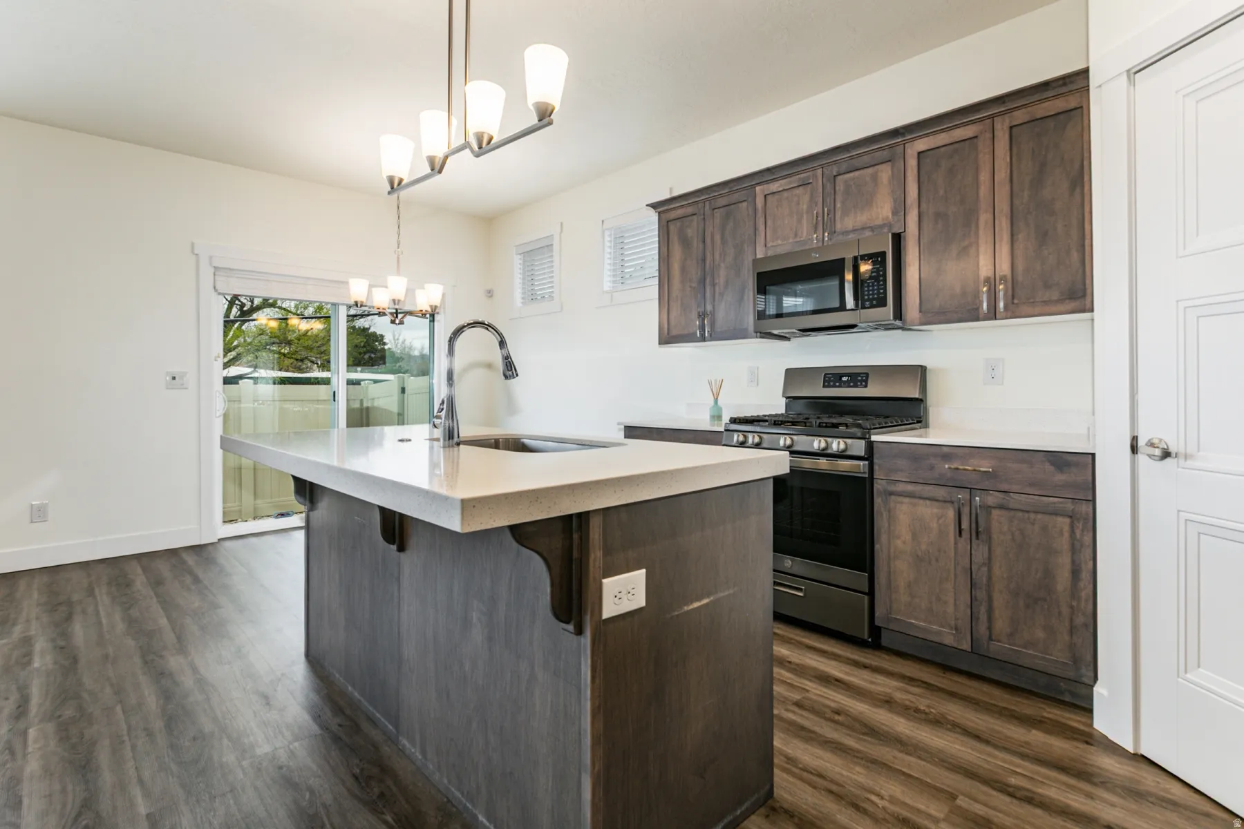 Kitchen featuring dark wood finish cabinets, stainless steel appliances, hanging lights, and a center island with sink