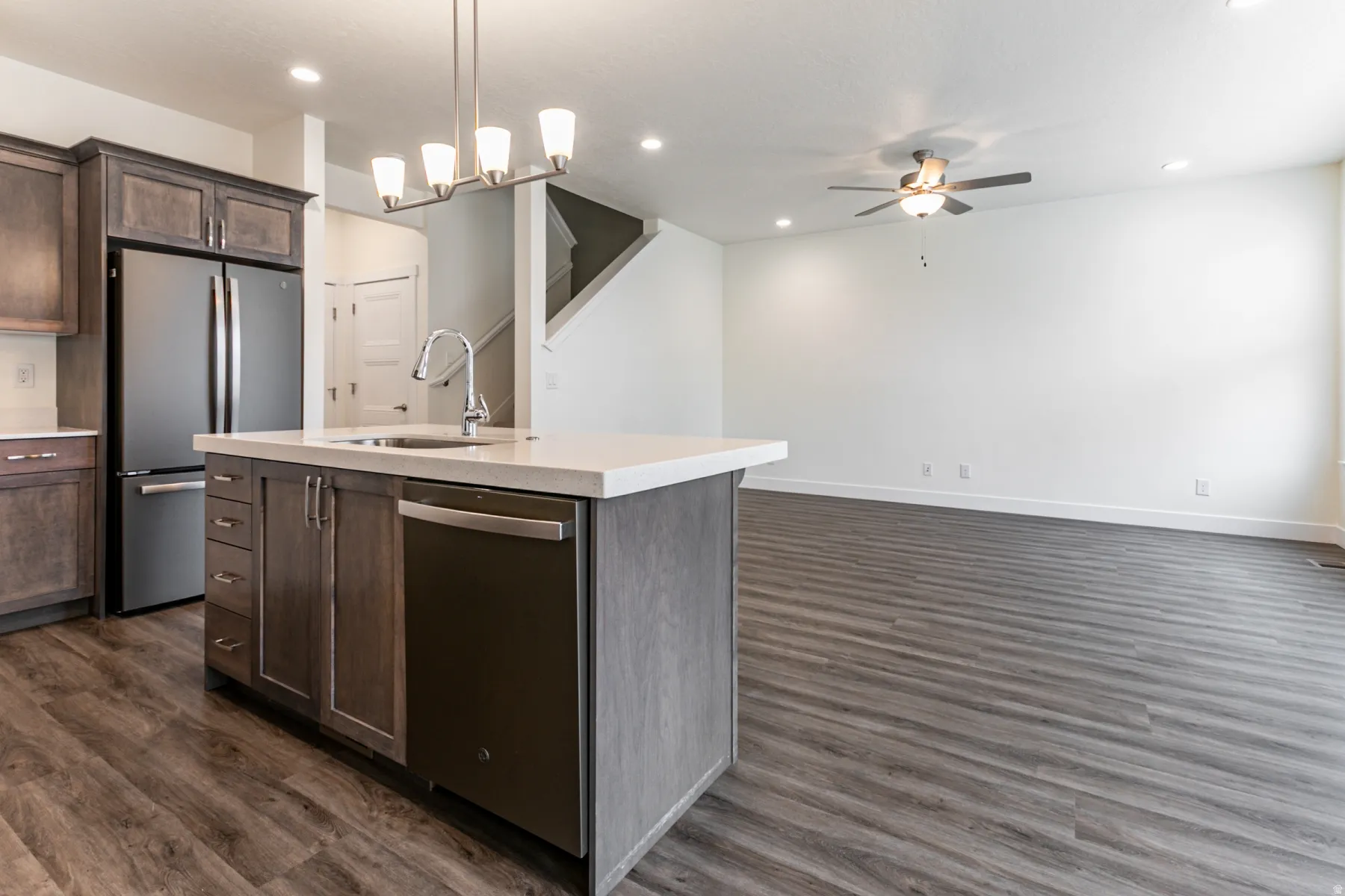 Kitchen featuring stainless steel appliances, dark wood finish cabinetry, dark wood-style floors, a ceiling fan, and a kitchen island with sink