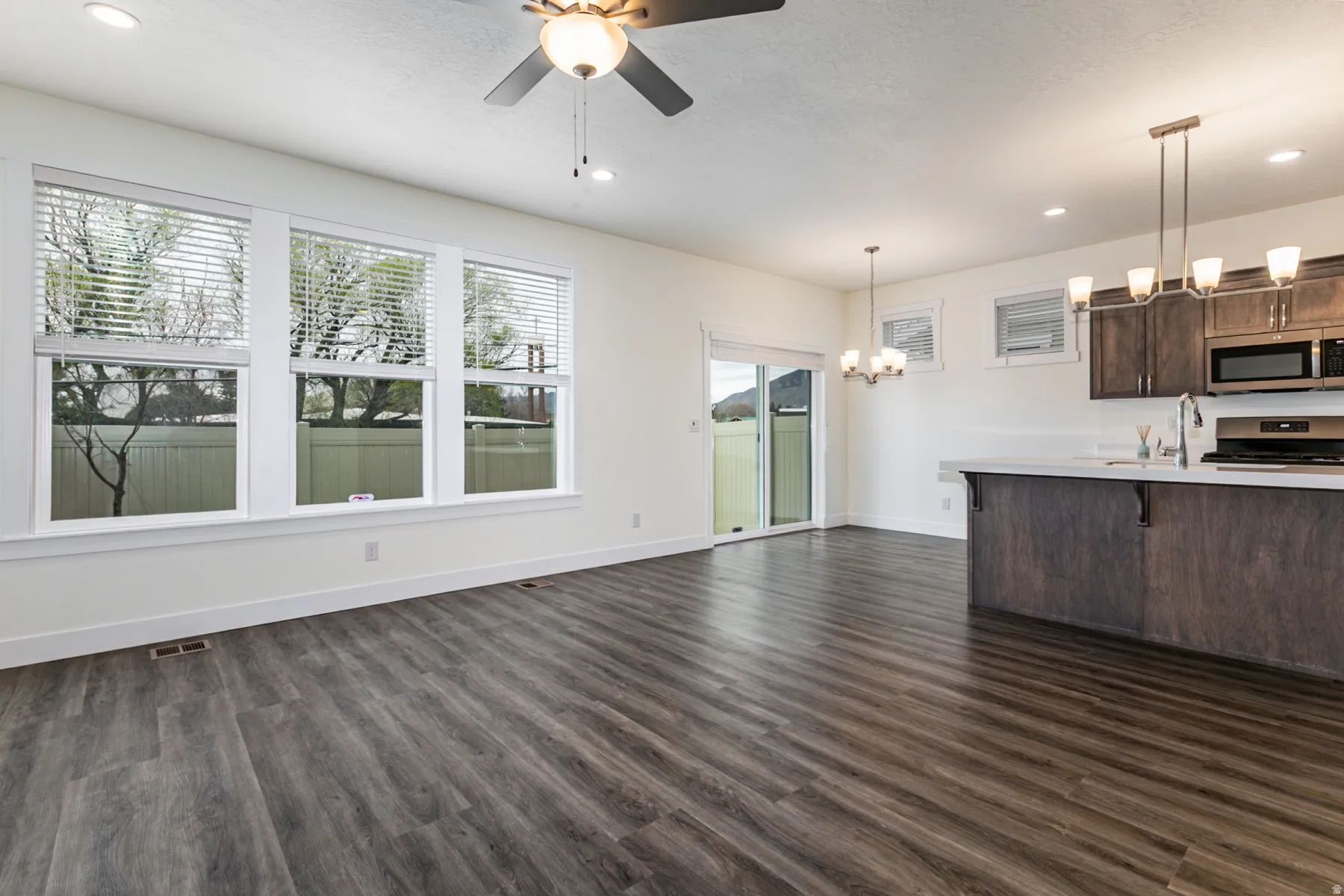 Kitchen with dark wood finish cabinets, a breakfast bar, stainless steel appliances, a ceiling fan, and hanging lights