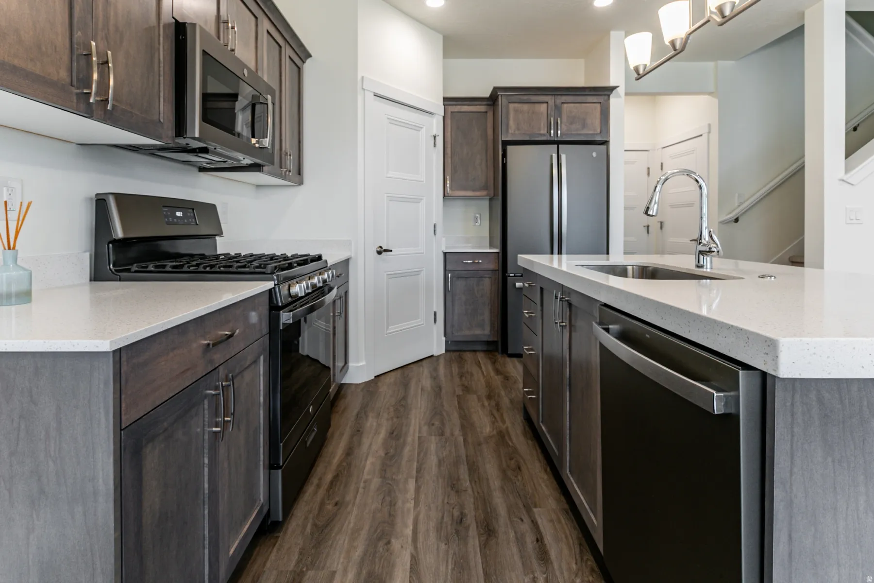 Kitchen featuring stainless steel appliances, light stone counters, dark wood-style flooring, and dark wood finish cabinets