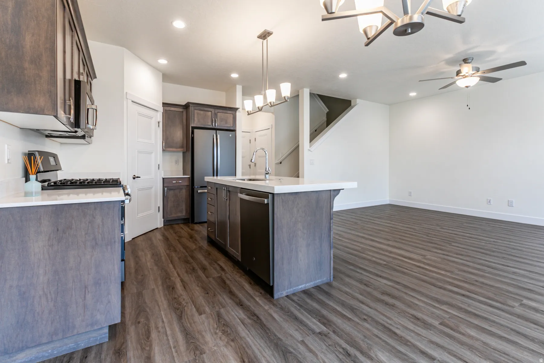 Kitchen featuring a chandelier, dark wood finish cabinetry, stainless steel appliances, dark wood-style flooring, and an island with sink