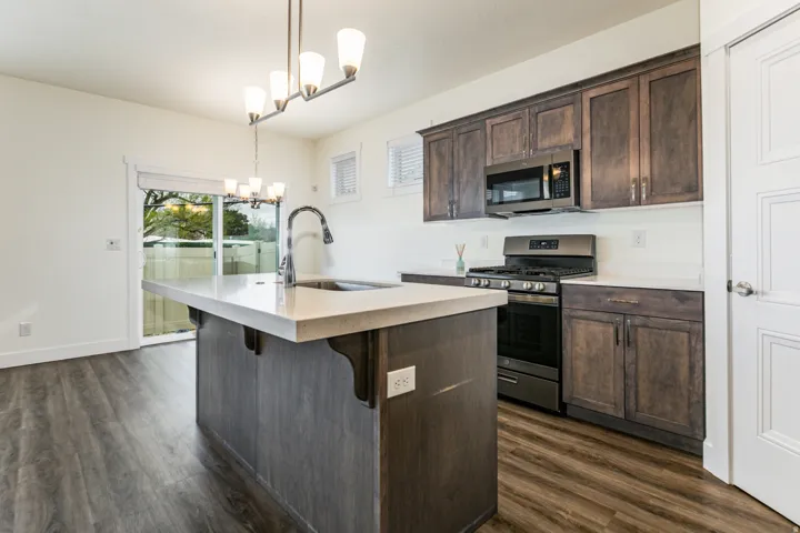 Kitchen featuring dark wood finish cabinets, stainless steel appliances, hanging lights, and a center island with sink