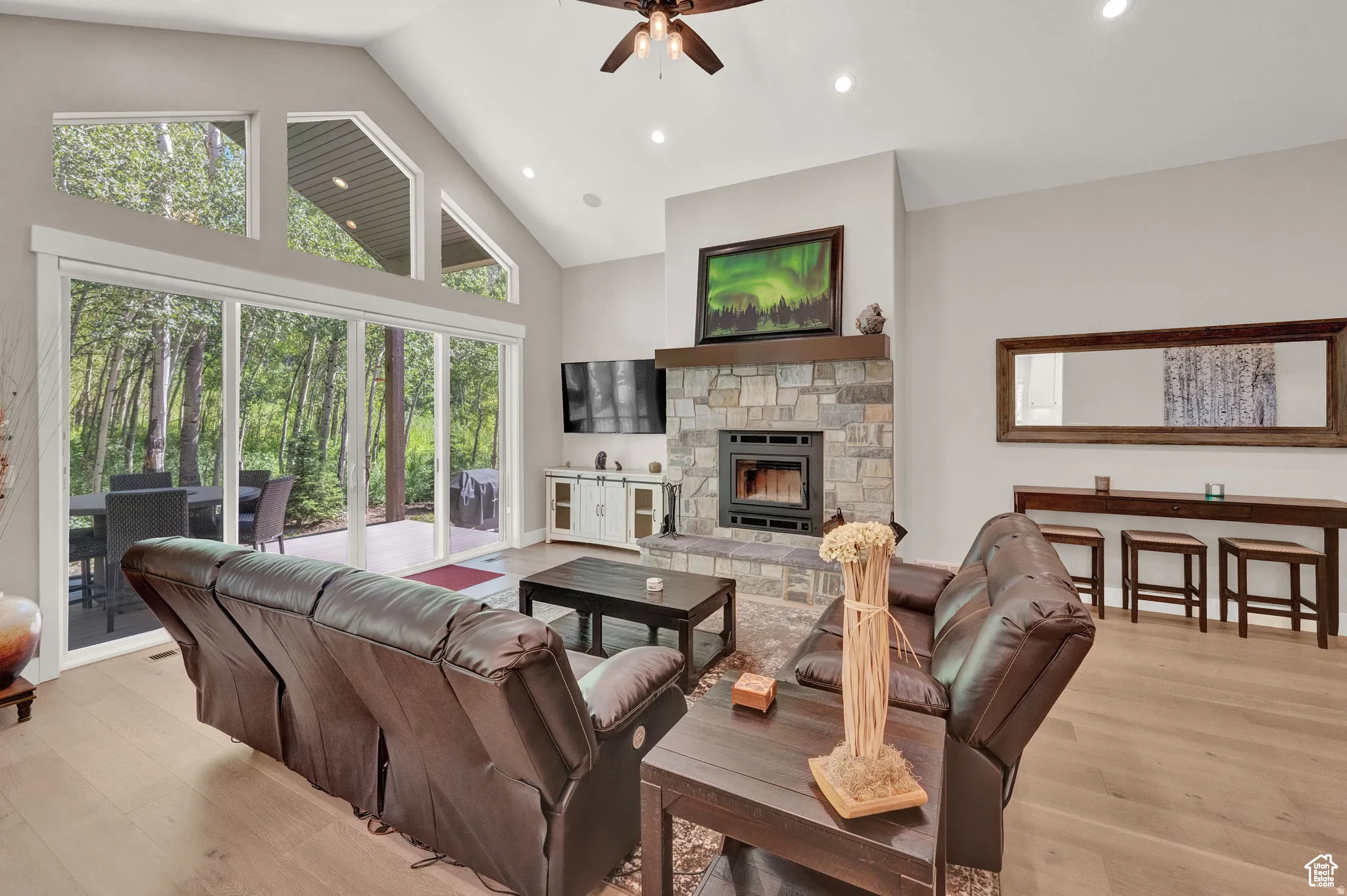 Living area with a stone fireplace, ceiling fan, a high ceiling, light wood-style floors, and recessed lighting