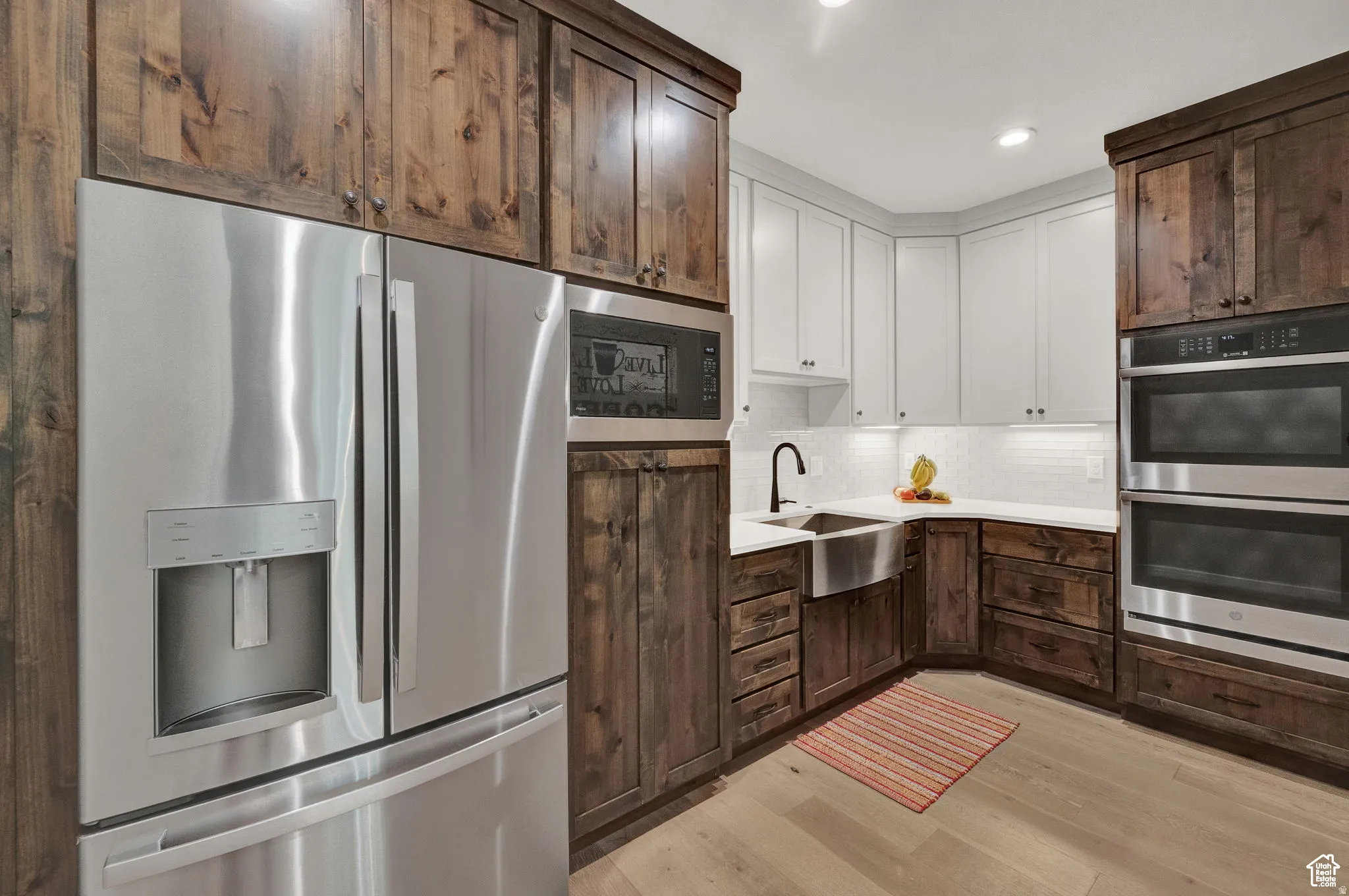 Kitchen with stainless steel appliances, tasteful backsplash, dual tone cabinetry, light wood finished floors, and recessed lighting