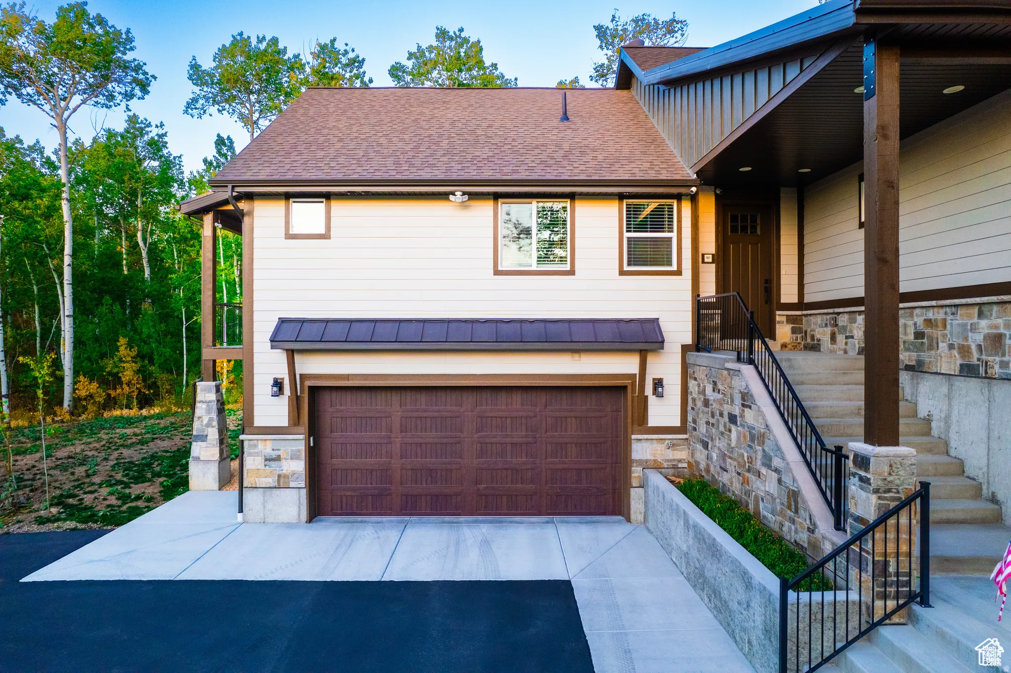 View of front of property with stone siding, a garage, a shingled roof, and driveway