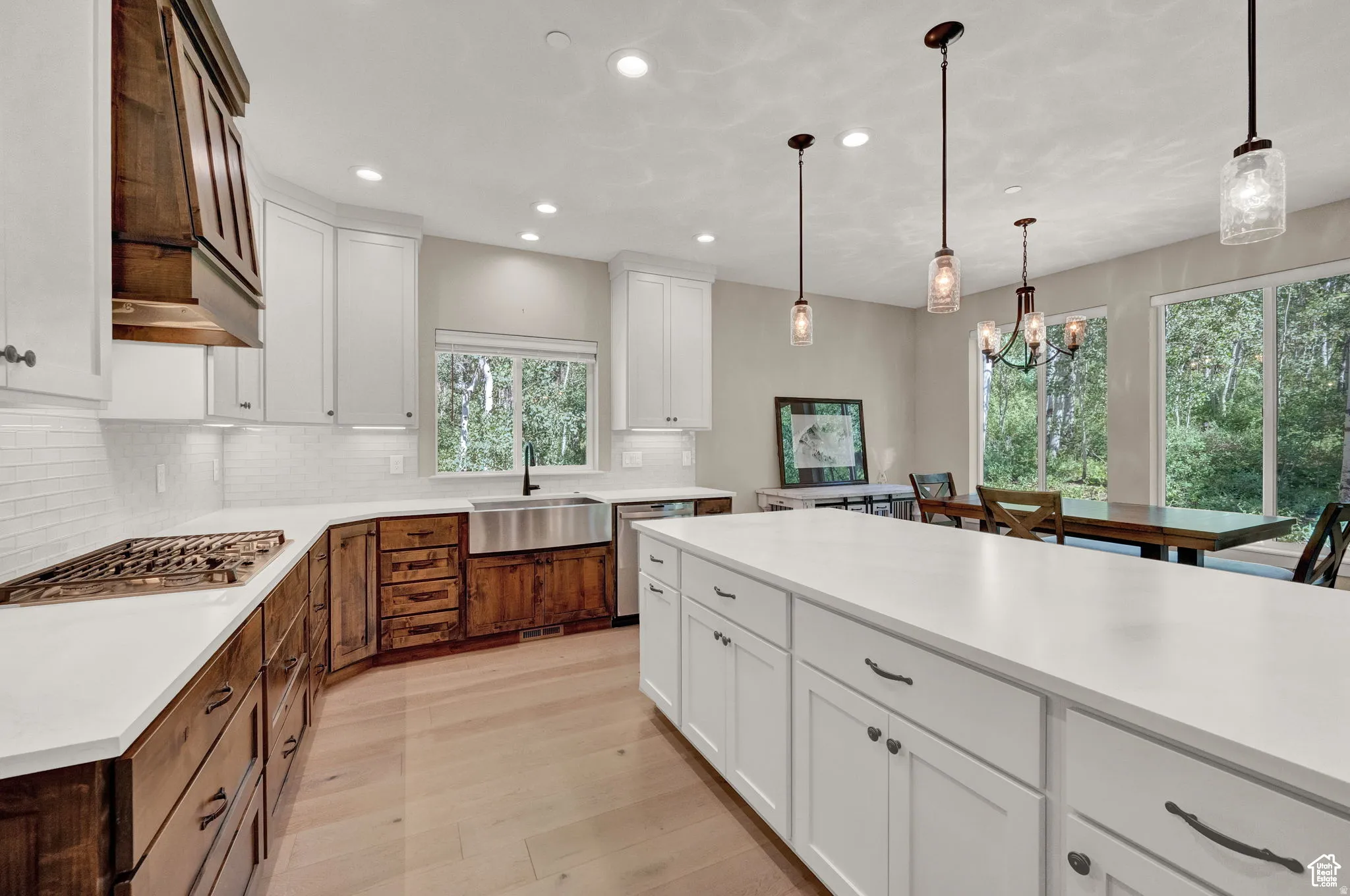 Dual tone kitchen with two tone cabinets, stainless steel appliances, light wood finished floors, decorative backsplash, and hanging lights