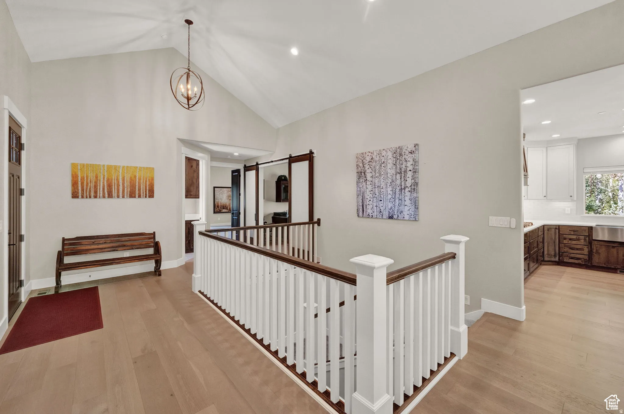 Corridor with light wood-style floors, vaulted ceiling, suspended lighting, and an upstairs landing