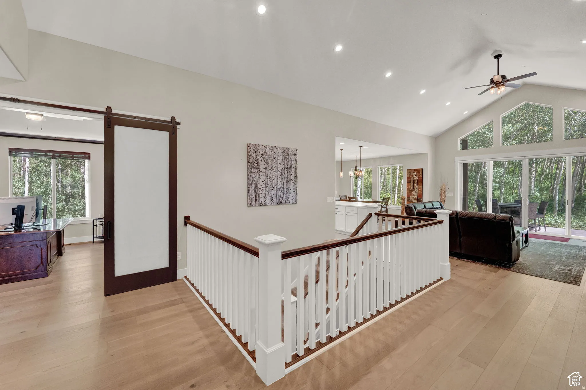 Hallway featuring an upstairs landing, light wood-style flooring, plenty of natural light, a high ceiling, and hanging lights