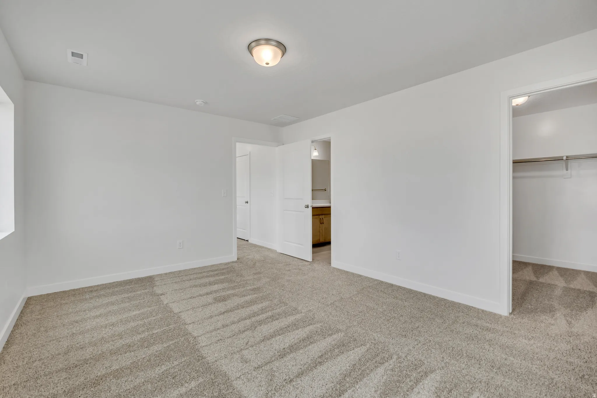 Unfurnished bedroom featuring a spacious closet, light colored carpet, and connected bathroom