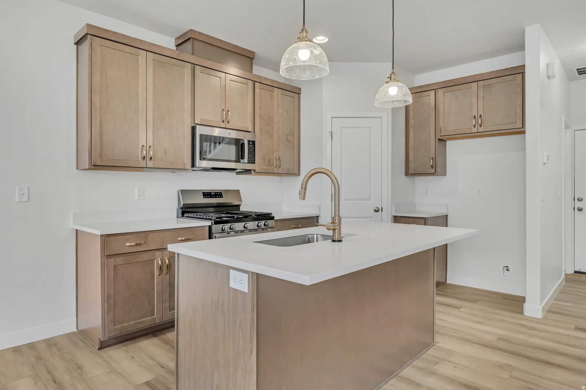 Kitchen with an island with sink, stainless steel appliances, hanging light fixtures, and light wood-style floors