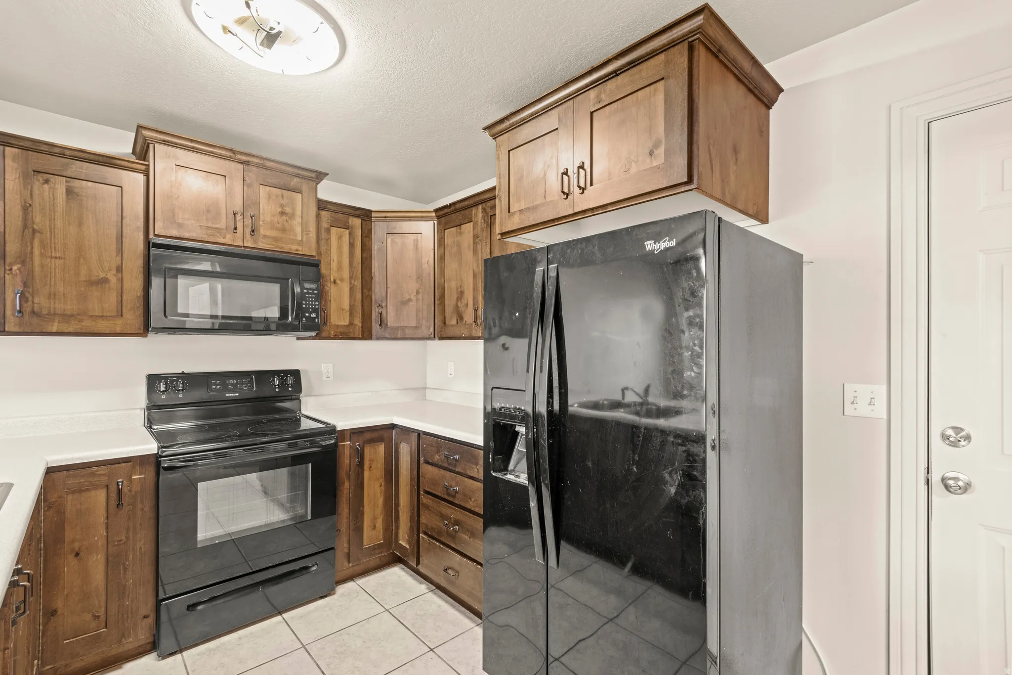Kitchen with black appliances, light countertops, light tile patterned flooring, and wood finish cabinetry