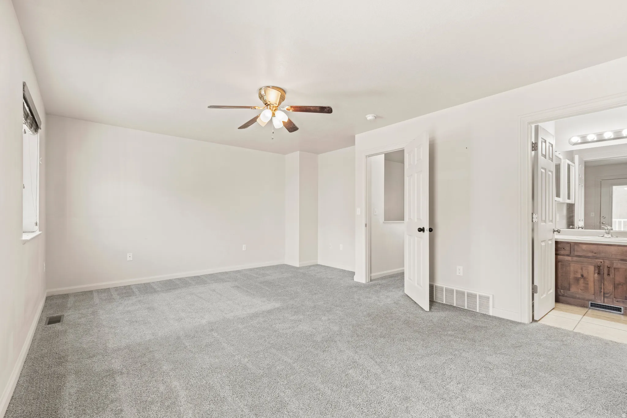 Unfurnished bedroom featuring light colored carpet, a ceiling fan, and ensuite bathroom